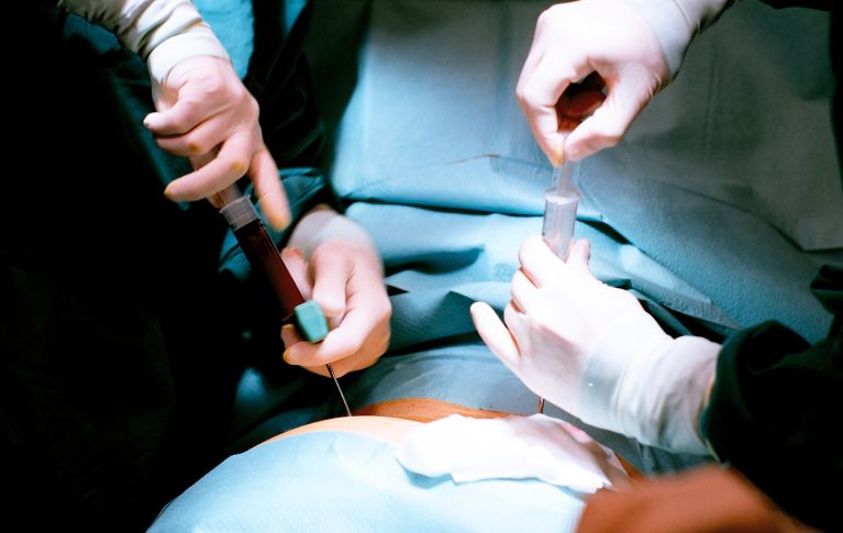 Operationssaal: Mit zwei Spritzen wird einer Person unter Vollnarkose Knochenmark entnommen