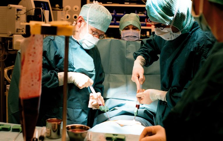 Operationssaal: Zwei Ärzte entnehmen einer einer Person unter Vollnarkose mit zwei grossen Spritzen Knochenmark